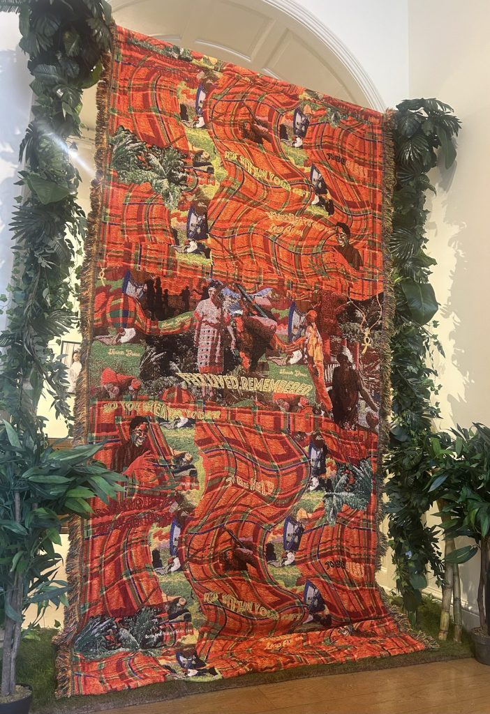 The image contains an intricate red and green textile piece by artist Tyreis Holder.