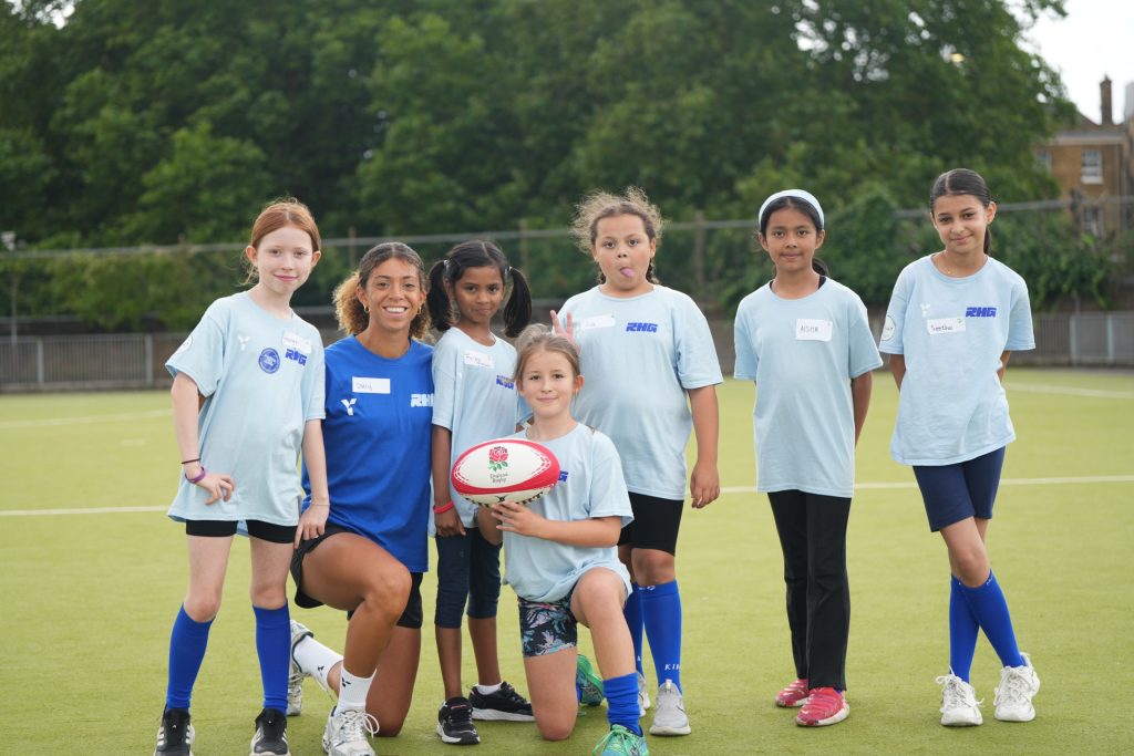 Darcy Bourne with a happy group of young girls at her charity Raising Her Game. The girl in the centre holds a rugby ball. 
