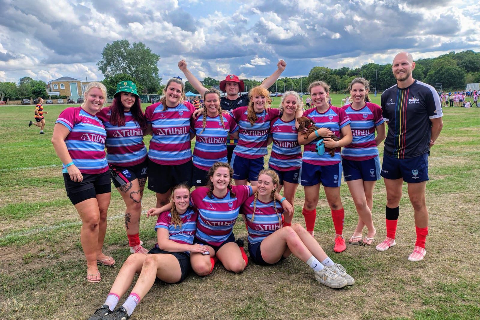 This is a team photo of the Wimbledon RFC Women's XV team looking happy after a match.