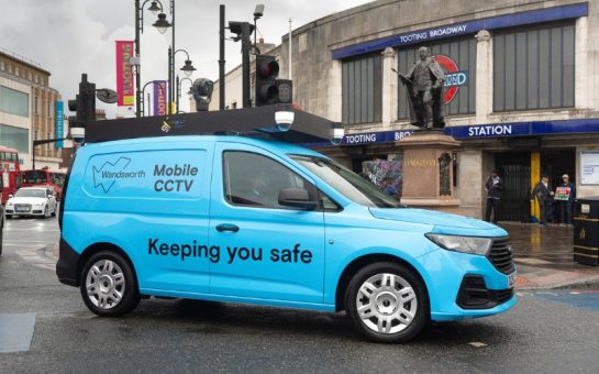 A blue Wandsworth Council mobile CCTV van driving past Tooting Broadway tube station.