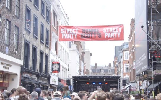 Sign of Ronnie Scott's street party hanging above the Soho venue, with an outside stage in the background.