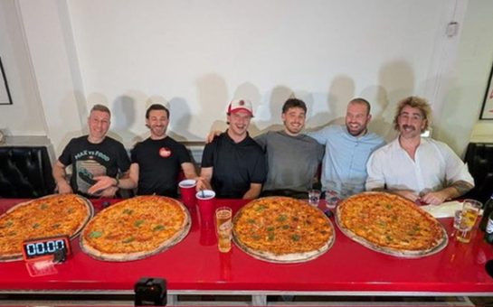 Six men sitting in front of a pizza