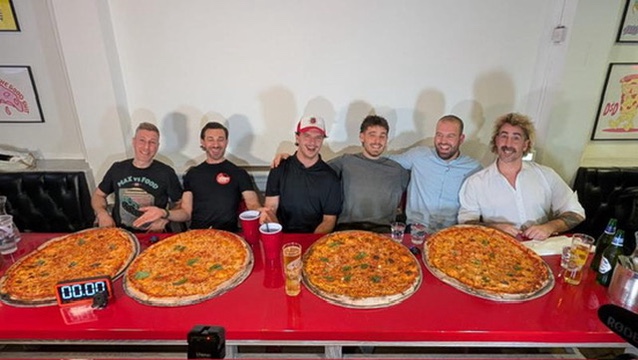 Six men sitting in front of a pizza