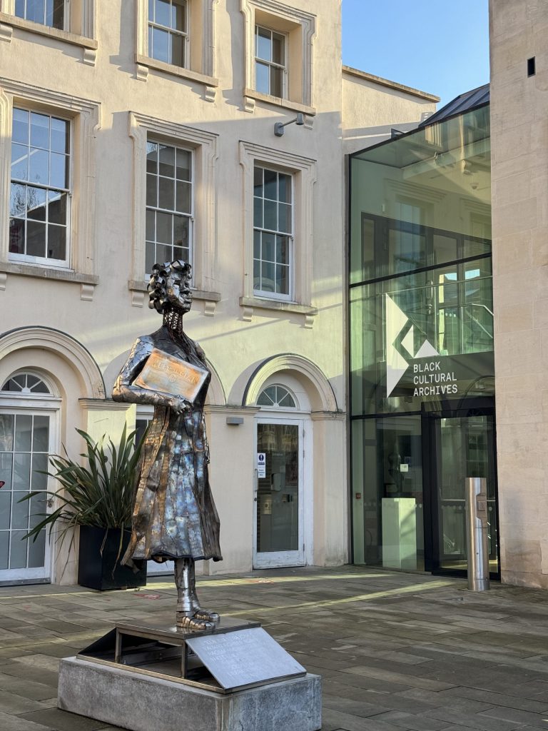 A photo of the exterior of Black Cultural archives in Brixton. It features a statue and an old building with glass windows.