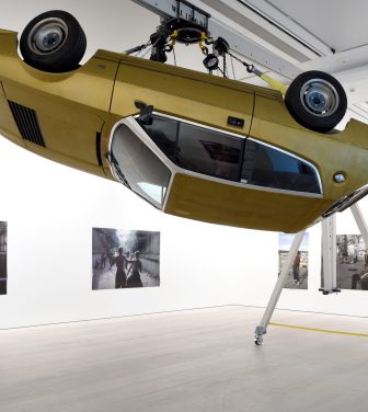 Installation in the Saatchi Gallery showing an upside down yellow car suspended in the air