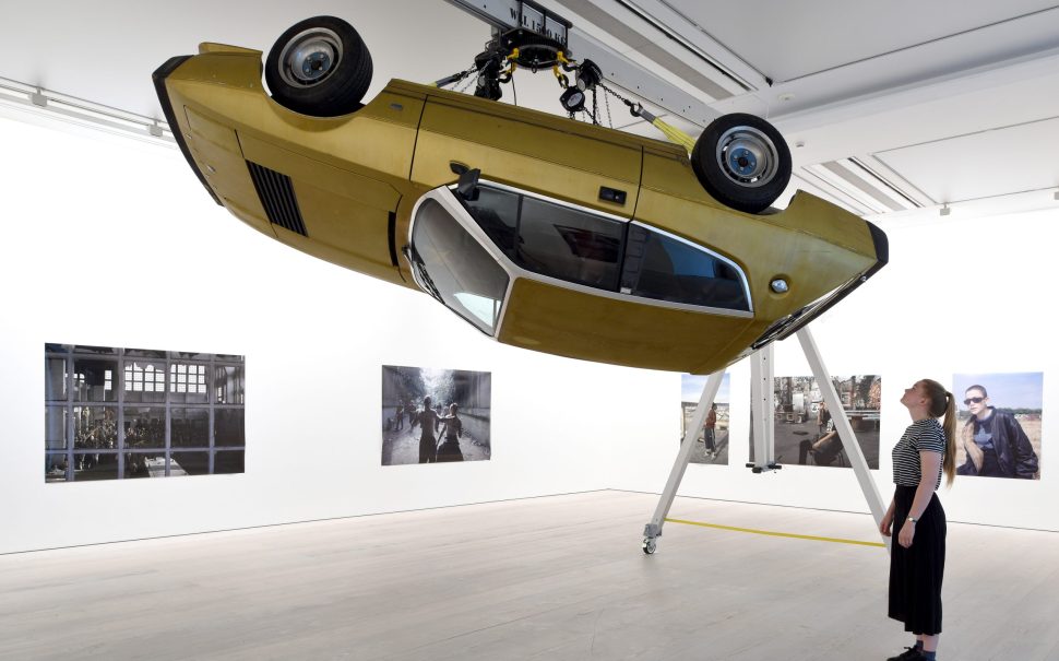 Installation in the Saatchi Gallery showing an upside down yellow car suspended in the air