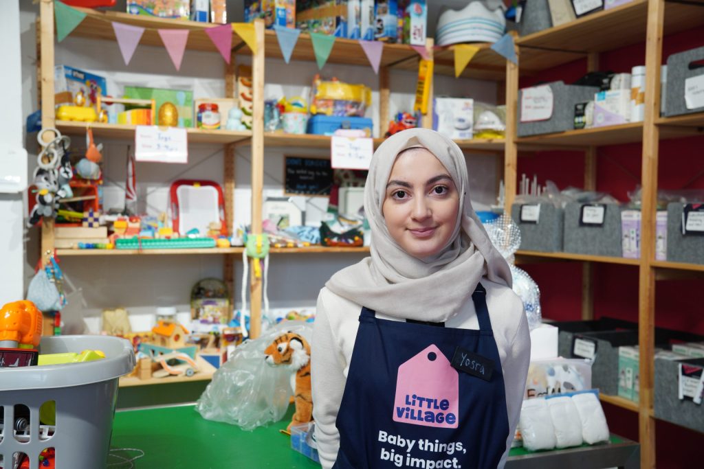 A picture of Yosr Bahr-Al-Ulum, a volunteer at Little Village baby bank. She is standing in the charity's Brent hub amongst shelves of their donated supplies.