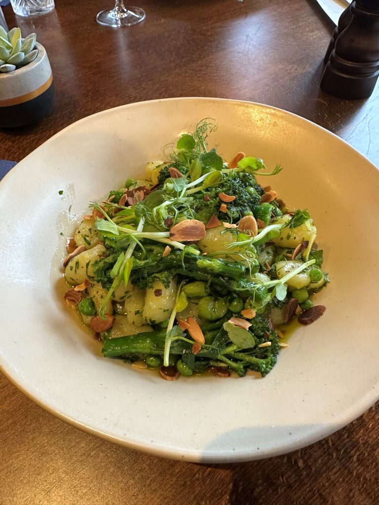 A bowl of confit garlic pesto gnocchi with peas, broad beans, purple sprouting broccoli and almonds.