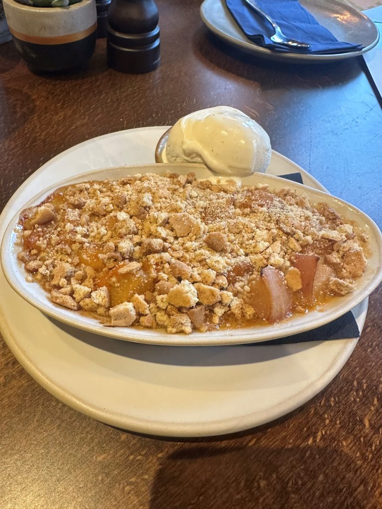 An oval dish full of peach & apricot crumble and a side of vanilla ice cream.