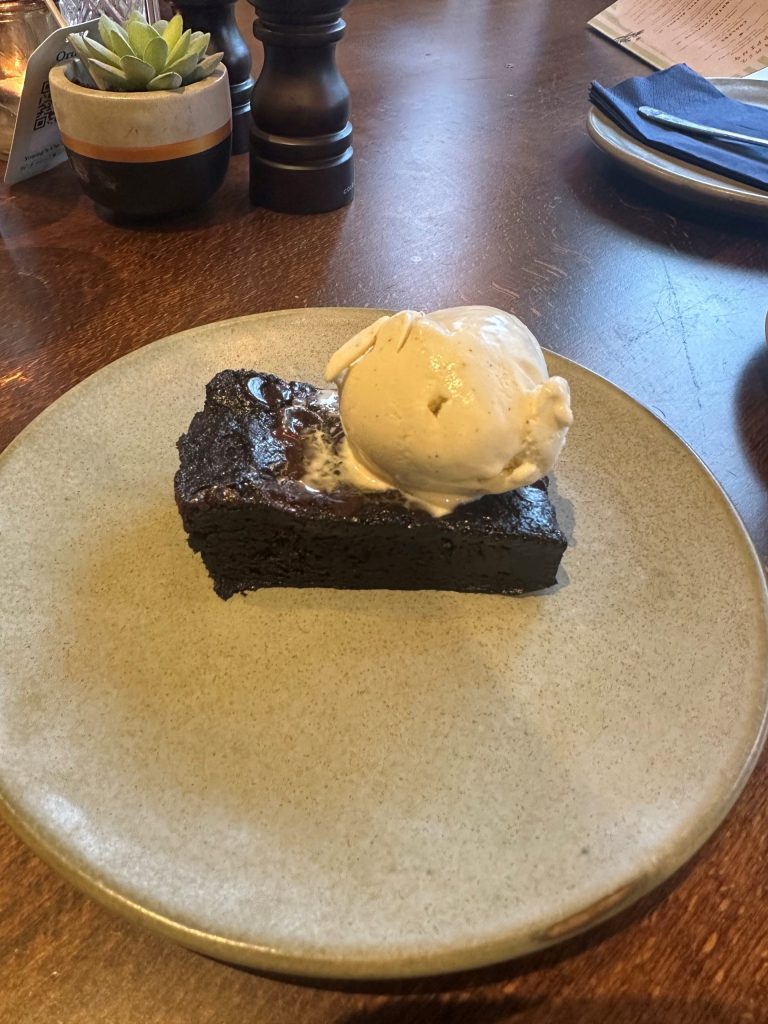A plate with a brownie and a scoop of vanilla ice cream on top at The Althorp.