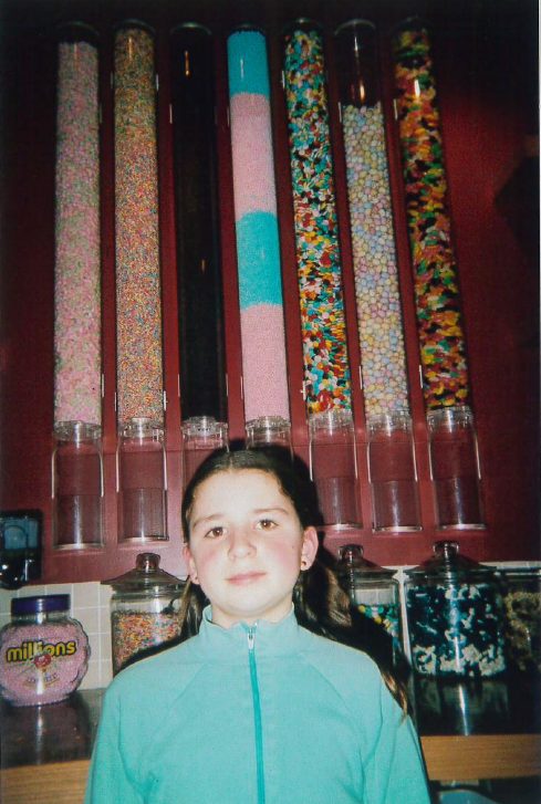 11-year-old Lucy with low bunchies and a green zip-up jacket in front of an old fashioned sweet store in a pub on Bellevue Road.