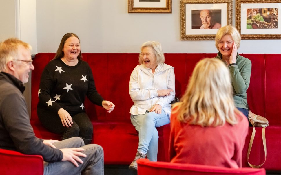 A group of over-50s acting class attendees, laughing together while in class