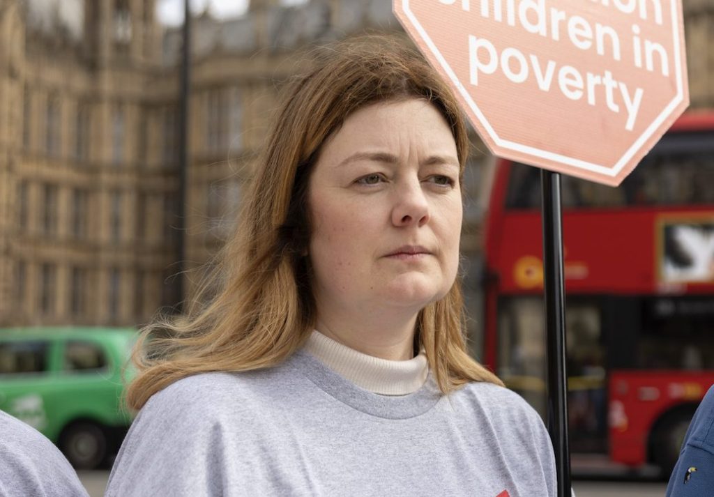 Rachel Walters, Coalition Manager at the charity End Child Poverty UK standing holding a sign as she campaigns outside Westminster.