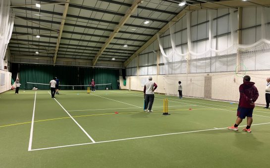 People playing cricket on an indoor tennis court