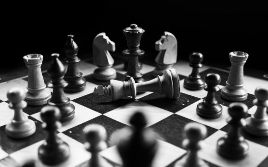 A chess board with pieces in a circle and a fallen King in the middle. Photo by Felix Mittermeier on Unsplash
