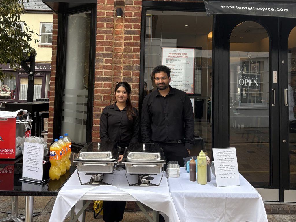 Two waiters dressed in black stand behind a food stand.