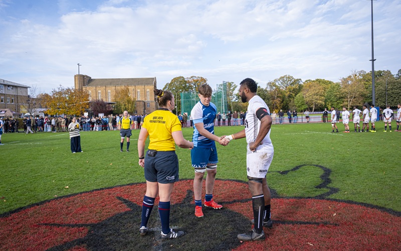 Captains of Royal Artillery and St Mary's University rugby team shaking hands on painted poppy in middle of the field before the remembrance match
