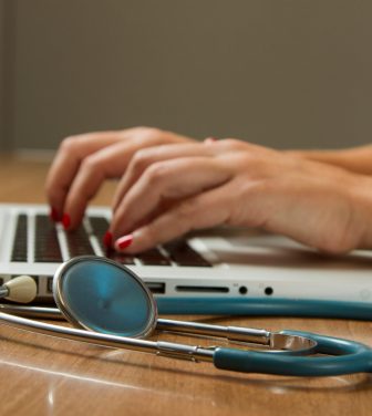 Woman's hands on computer typing next to stethoscope