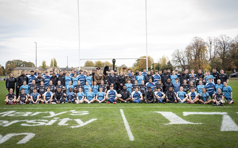 St Mary's University and Royal Artillery rugby teams pose for team photo ahead of remembrance match under goal post with cannon behind them