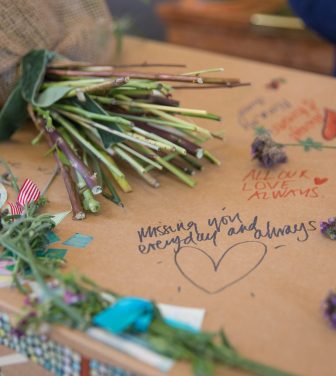 Cardboard coffin with handwritten tributes, flowers, and messages.