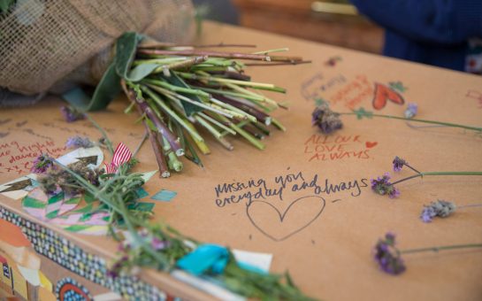 Cardboard coffin with handwritten tributes, flowers, and messages.