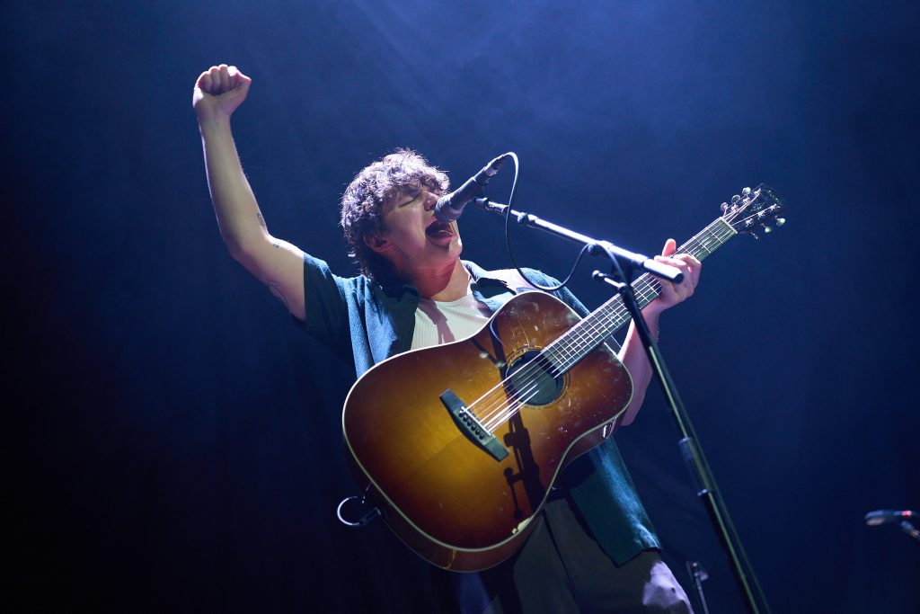 Man performs on stage with a fist in the air while playing a guitar