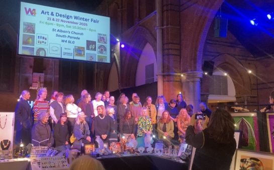 A group of artists standing on a stage under a projector screen reading "W4 Winter Art and Design Fair"