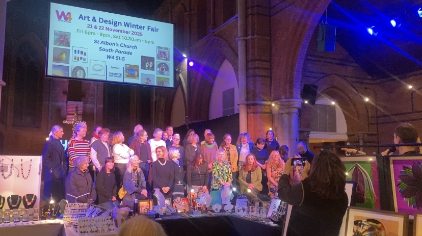 A group of artists standing on a stage under a projector screen reading "W4 Winter Art and Design Fair"