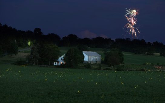 Fireworks going off over a field and farm