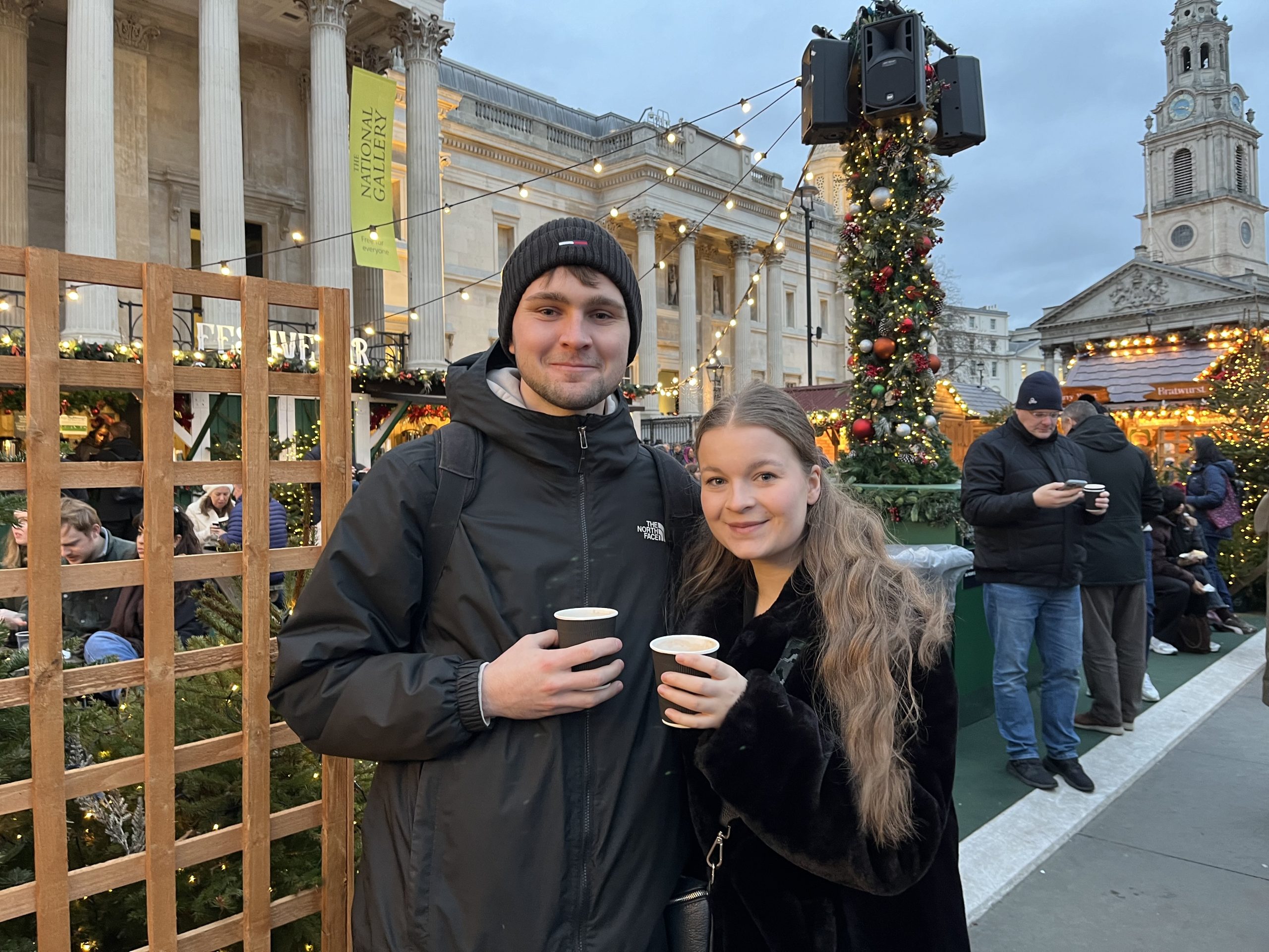 A couple hold disposable coffee cups in a Christmas market in front of the National Gallery in London.