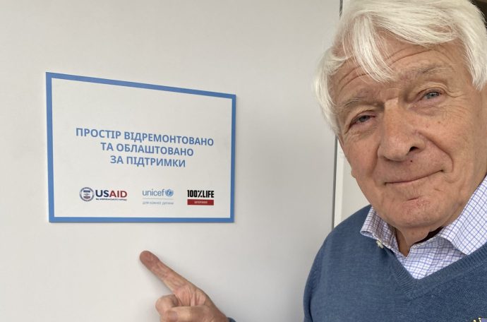 Robin Jowit pointing towards a sign with different aid organisations on it.