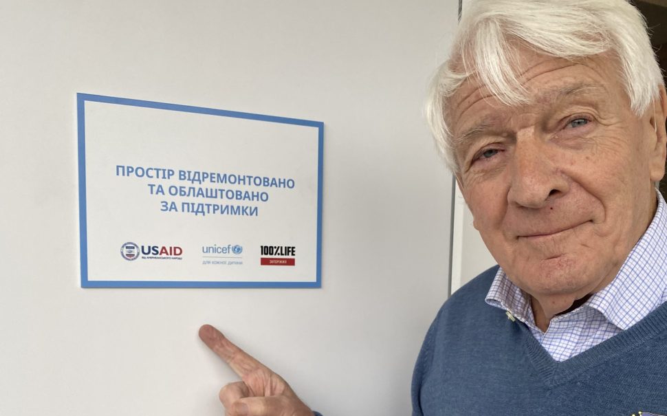 Robin Jowit pointing towards a sign with different aid organisations on it.