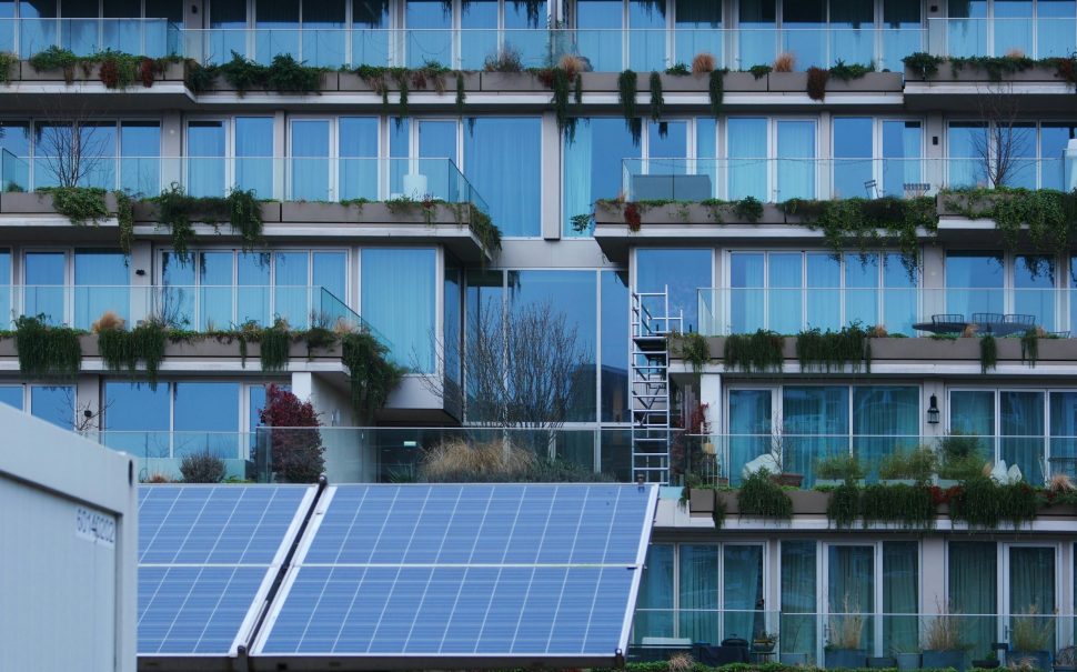 A large solar panel in front of a modern building with balconies and plants.