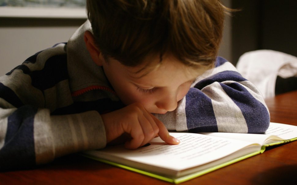 Young child reading a book with his finger on the page.