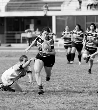 The photograph is of female rugby players. One lady attempting to tackle another while she is running with the ball.