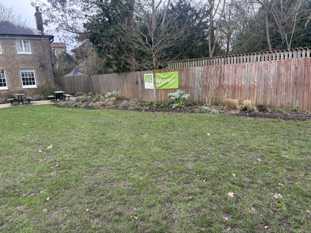 Green Flag winner banner on display at Marble Hill park, Twickenham, on a fence behind grass lawn and flower bed.