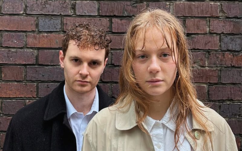 Photo of the two actors in the play. One man and one woman dressed in office clothing.