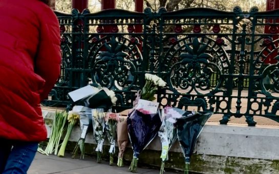 Woman leaning down in front of flowers at vigil