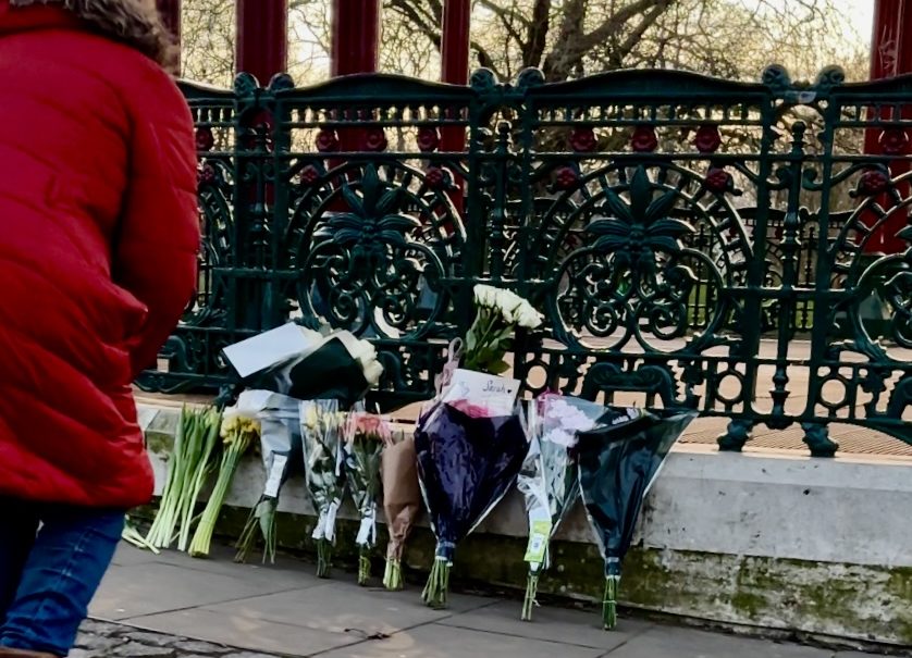 Woman leaning down in front of flowers at vigil