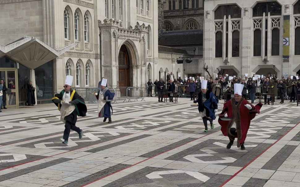 People wearing Chefs hats and cloaks running and flipping pancakes