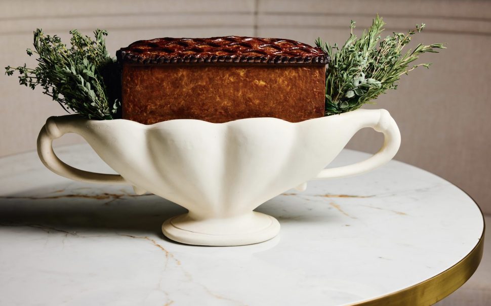 A rectangular pie in a white dish filled with herbs on a round marble table