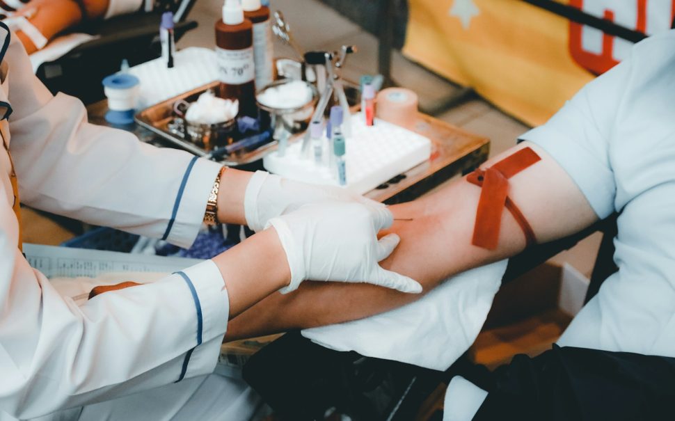 A person having a needle inserted into their arm by a doctor, for the purpose of giving blood.