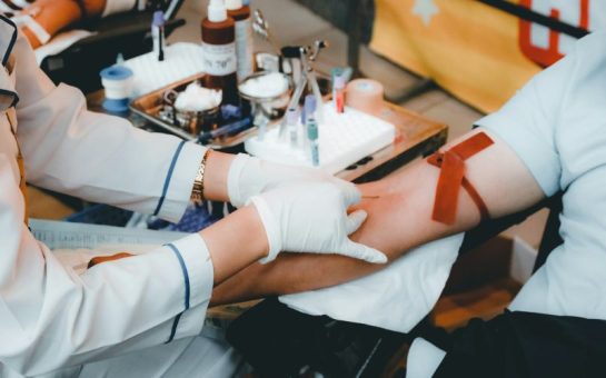 A person having a needle inserted into their arm by a doctor, for the purpose of giving blood.