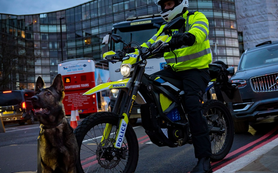 A met police officer sits on a police-marked e-bike with a police Alsatian sitting in the foreground.