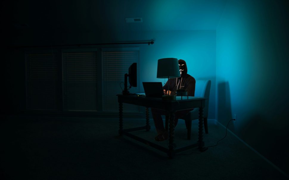 An anonymous person sitting at a computer in a dark room.