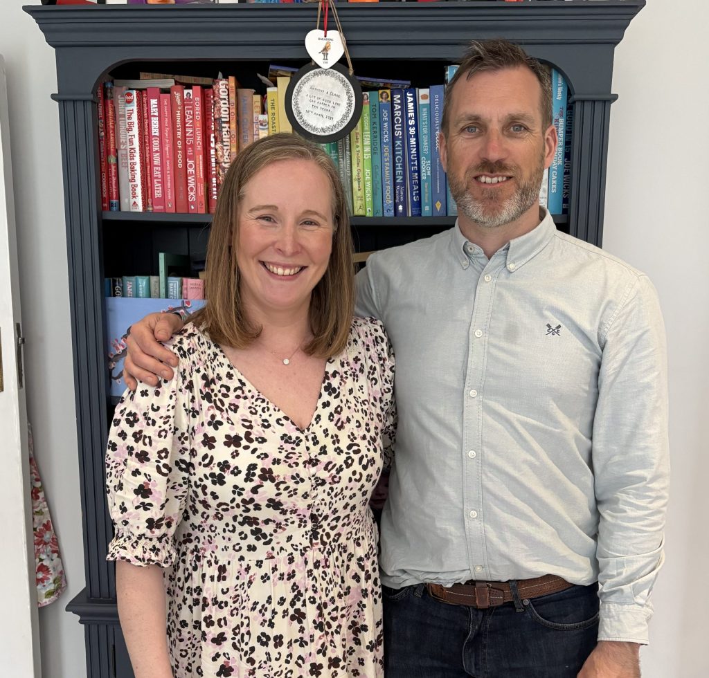 A husband and wife standing in front of a bookcase.