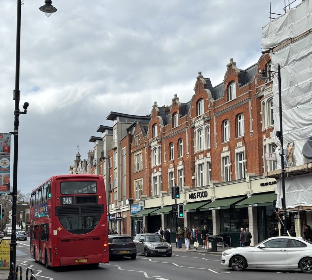 High street with large bus and cars, with big supermarket shown. 