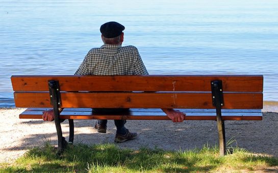 Elderly man sitting alone on a park bench by the water