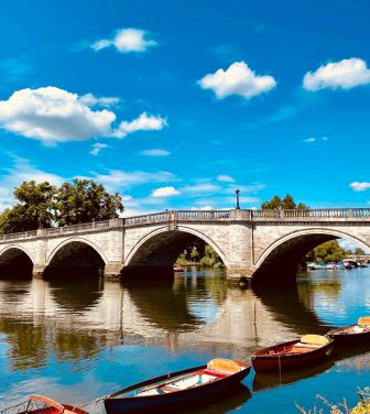 A photo of Richmond Bridge with small boats in front, and a blue sky with clouds