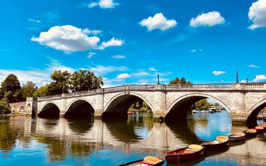 A photo of Richmond Bridge with small boats in front, and a blue sky with clouds